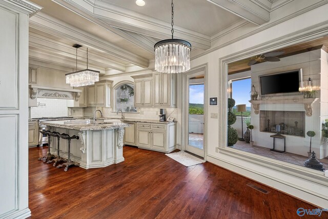 kitchen with tasteful backsplash, dark hardwood / wood-style flooring, a kitchen island with sink, cream cabinets, and a kitchen bar