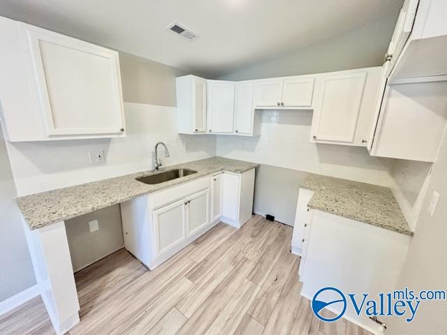 kitchen with sink, vaulted ceiling, white cabinets, light stone counters, and light hardwood / wood-style floors