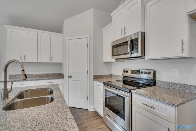 kitchen featuring light stone counters, white cabinets, a sink, stainless steel appliances, and wood finished floors