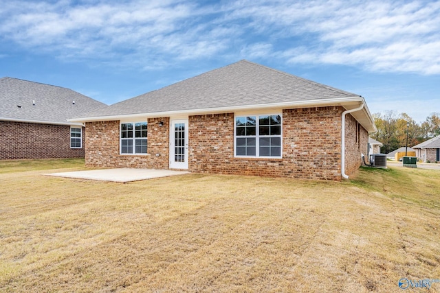 rear view of house featuring brick siding, a patio, roof with shingles, central AC, and a lawn