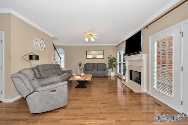 living room with ornamental molding, ceiling fan, a fireplace, and light hardwood / wood-style flooring