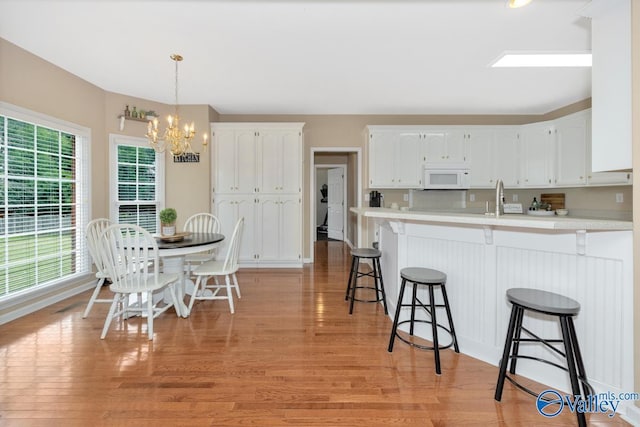 kitchen featuring white cabinets, a chandelier, a kitchen breakfast bar, hanging light fixtures, and light hardwood / wood-style flooring