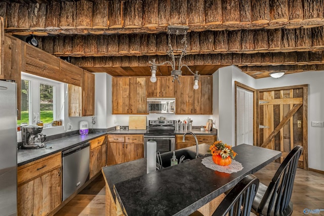 kitchen with appliances with stainless steel finishes, a kitchen island, sink, and light hardwood / wood-style flooring