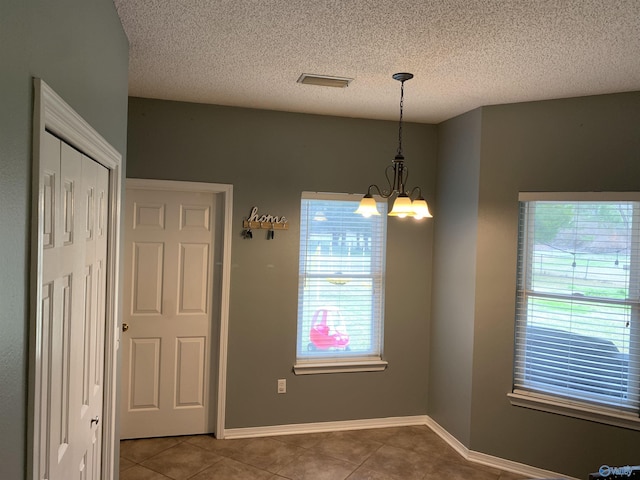 unfurnished dining area with a notable chandelier, tile patterned floors, and a textured ceiling