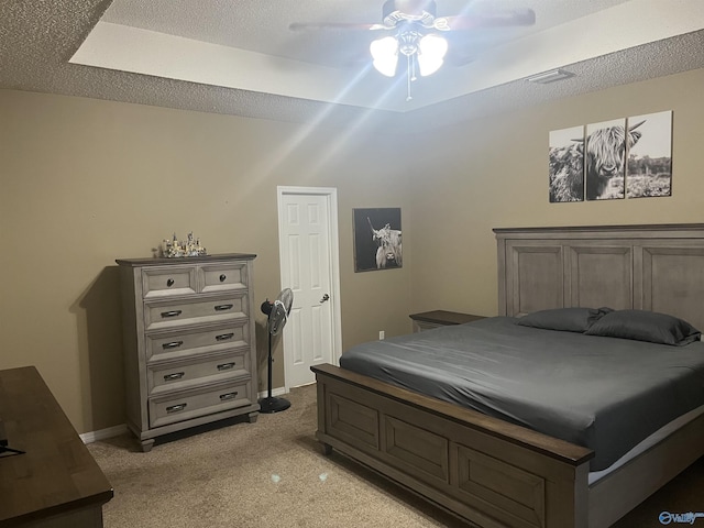 bedroom featuring light carpet, ceiling fan, a tray ceiling, and a textured ceiling