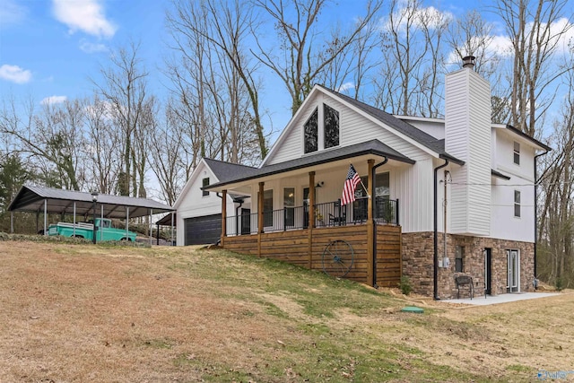 view of side of property featuring a chimney, a porch, a lawn, a garage, and stone siding