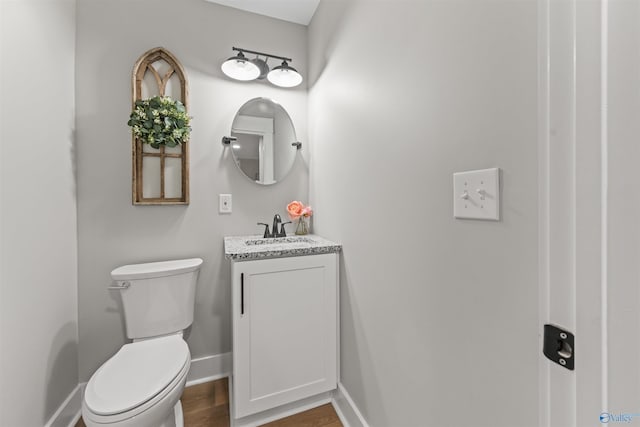 half bath with wood finished floors, vanity, toilet, and baseboards