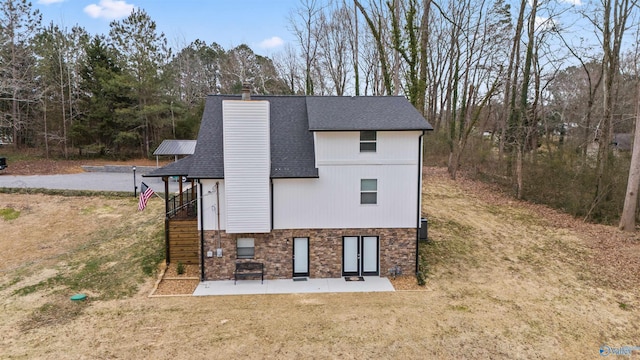 view of front of house featuring roof with shingles, a chimney, a front yard, a patio area, and stone siding