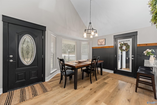 dining space with baseboards, light wood-style flooring, high vaulted ceiling, and a notable chandelier