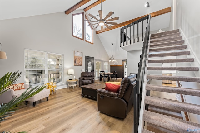 living area with beam ceiling, stairway, light wood finished floors, and ceiling fan with notable chandelier