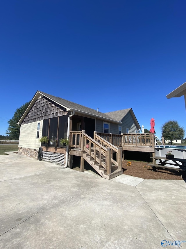 rear view of property featuring a sunroom, a patio, and a wooden deck