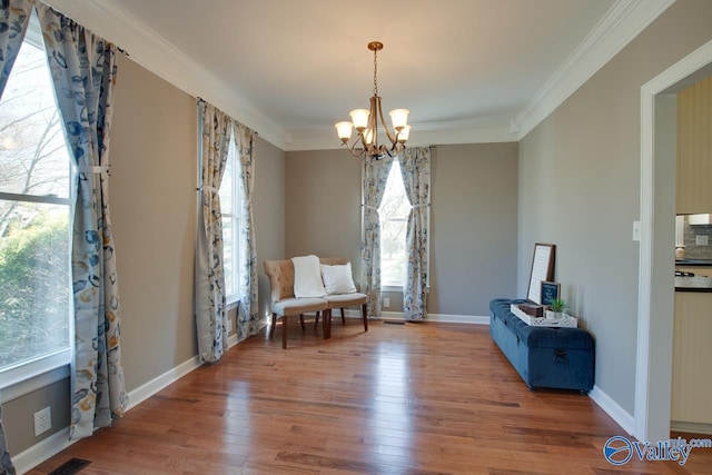 living area with ornamental molding, a notable chandelier, baseboards, and wood finished floors