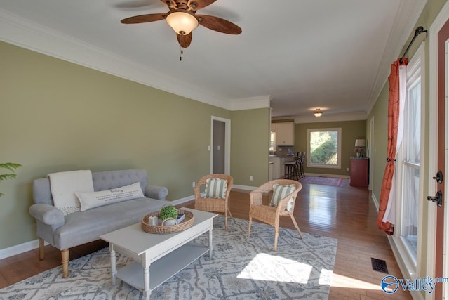 living room with baseboards, light wood-type flooring, visible vents, and crown molding