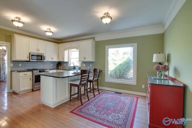 kitchen featuring light wood finished floors, appliances with stainless steel finishes, dark countertops, and white cabinetry