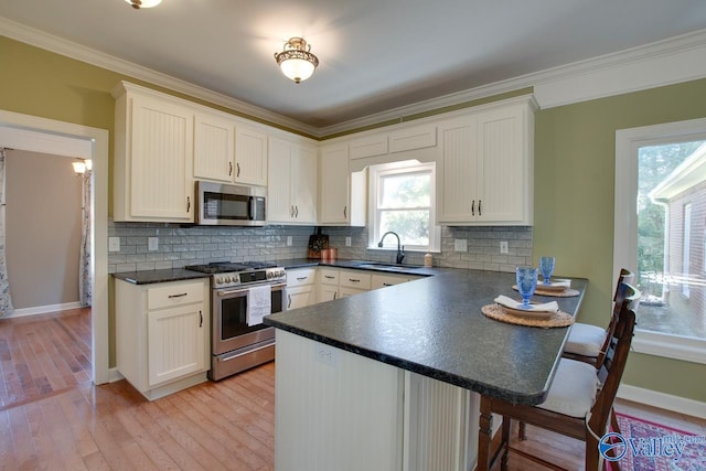 kitchen featuring appliances with stainless steel finishes, dark countertops, a sink, and crown molding