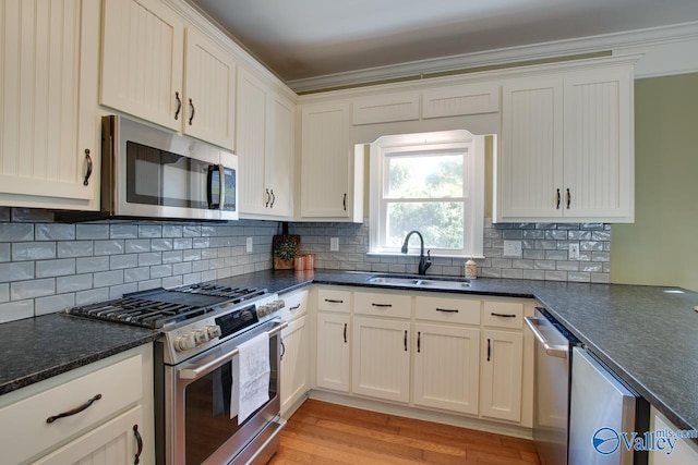 kitchen featuring a sink, appliances with stainless steel finishes, light wood-type flooring, tasteful backsplash, and crown molding