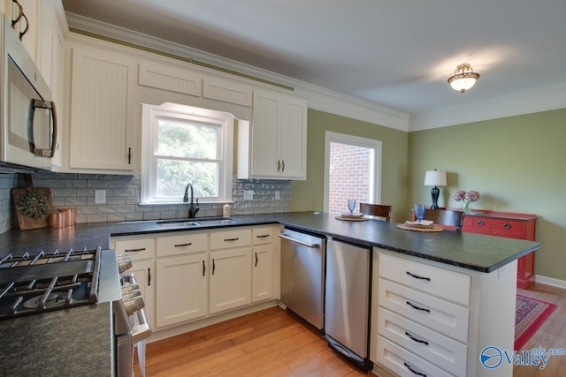 kitchen featuring light wood-style flooring, appliances with stainless steel finishes, ornamental molding, a peninsula, and a sink