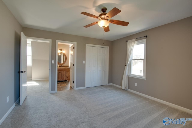 unfurnished bedroom featuring light carpet, baseboards, a ceiling fan, ensuite bathroom, and a sink