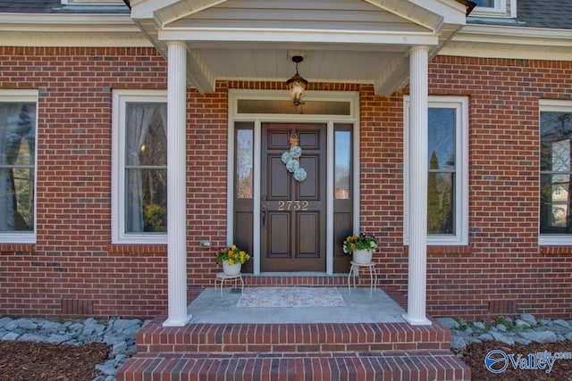 doorway to property with covered porch, roof with shingles, and brick siding