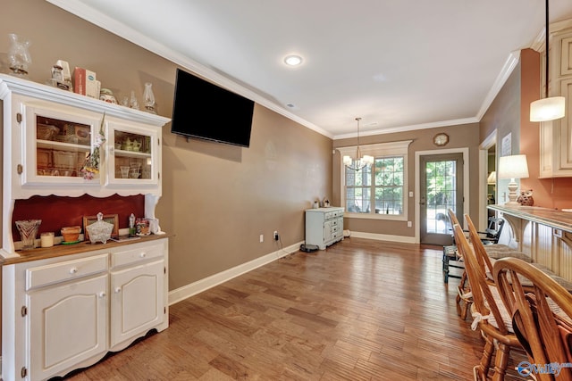 interior space featuring light wood finished floors, ornamental molding, a chandelier, and baseboards