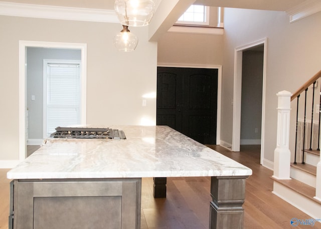 kitchen featuring hardwood / wood-style floors, crown molding, light stone countertops, and pendant lighting