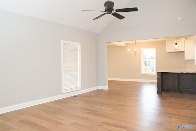 unfurnished living room with ceiling fan with notable chandelier, light hardwood / wood-style flooring, and high vaulted ceiling