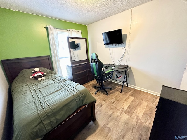 bedroom with light wood-type flooring, baseboards, and a textured ceiling