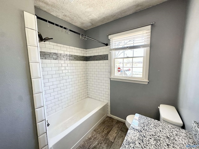 bathroom with baseboards, toilet, wood finished floors, a textured ceiling, and washtub / shower combination