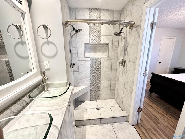 full bathroom with a sink, tiled shower, a textured ceiling, and double vanity