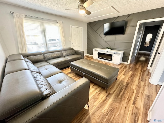 living room featuring baseboards, a textured ceiling, light wood-style flooring, and a ceiling fan