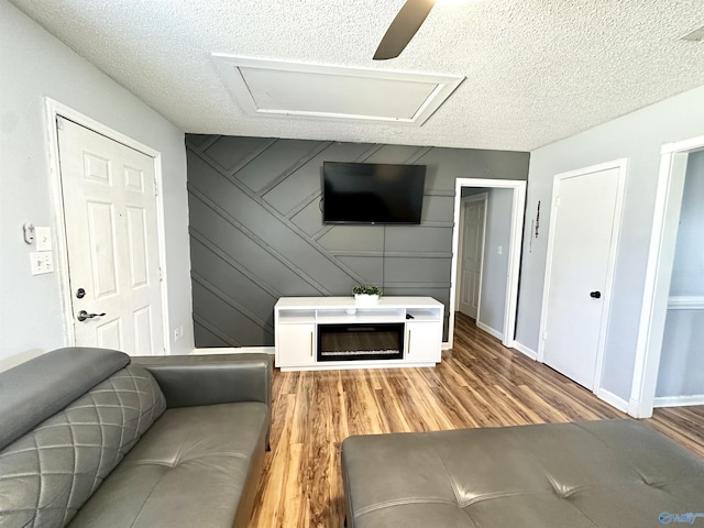 living room with light wood-type flooring, baseboards, a textured ceiling, and attic access