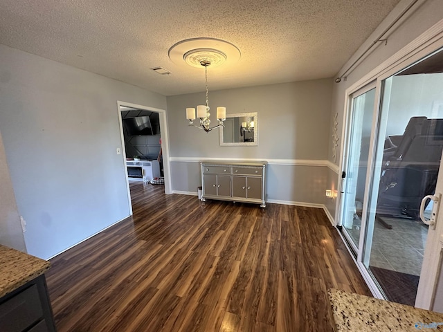 unfurnished dining area with a notable chandelier, a textured ceiling, baseboards, and dark wood-style flooring