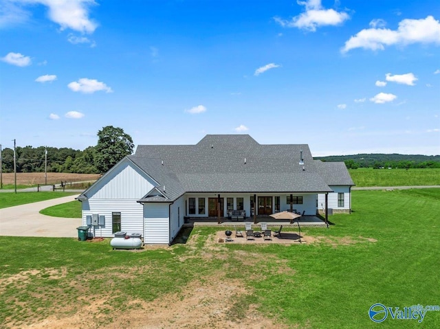 rear view of property featuring driveway, roof with shingles, board and batten siding, a patio area, and a yard
