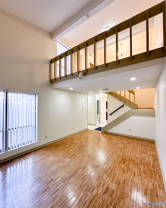 unfurnished living room featuring a towering ceiling, hardwood / wood-style floors, and beam ceiling