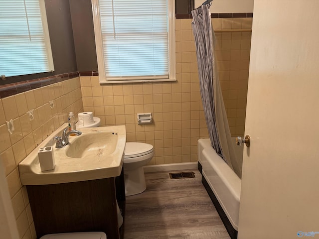 full bathroom with tasteful backsplash, hardwood / wood-style flooring, tile walls, shower / bath combo with shower curtain, and toilet