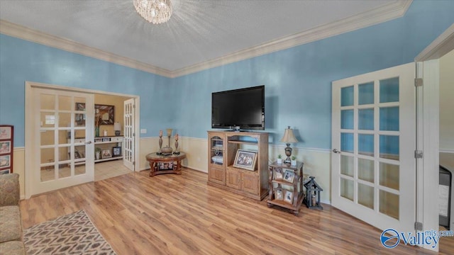 living area featuring wood finished floors, crown molding, french doors, and a wainscoted wall