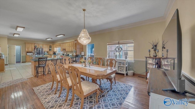 dining space featuring light wood-style floors, an inviting chandelier, crown molding, and a textured ceiling