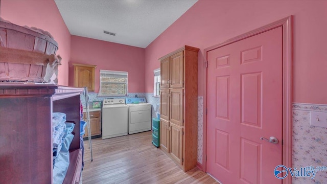 laundry room featuring visible vents, light wood finished floors, washing machine and clothes dryer, wainscoting, and a textured ceiling