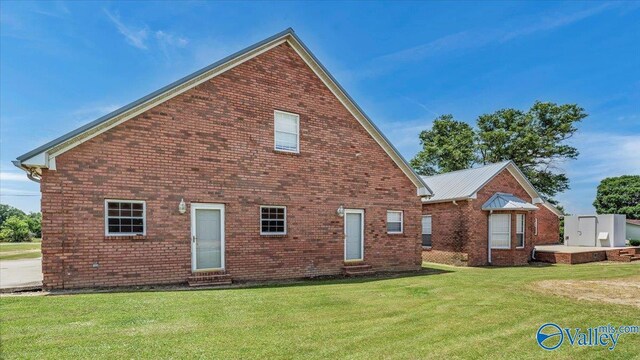 rear view of property featuring brick siding, a lawn, and entry steps