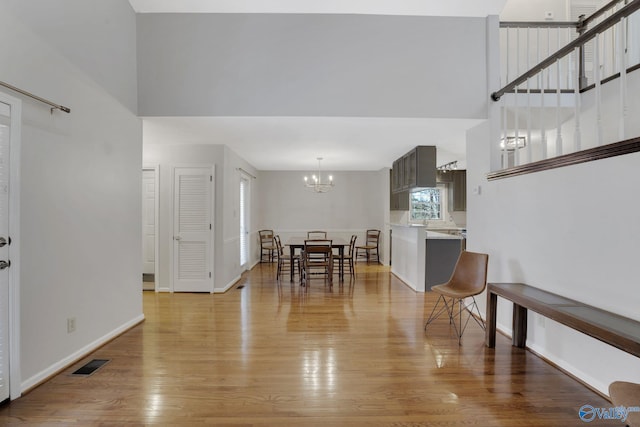 dining room featuring a chandelier, a high ceiling, visible vents, baseboards, and light wood-type flooring