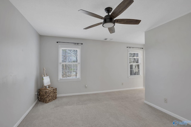 spare room featuring carpet floors, a ceiling fan, visible vents, and baseboards