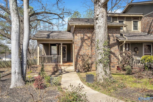 entrance to property with a porch, brick siding, and fence