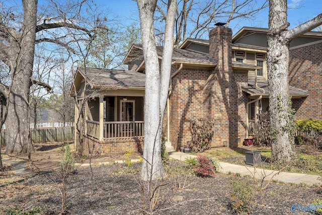 view of side of property featuring covered porch, a chimney, fence, and brick siding