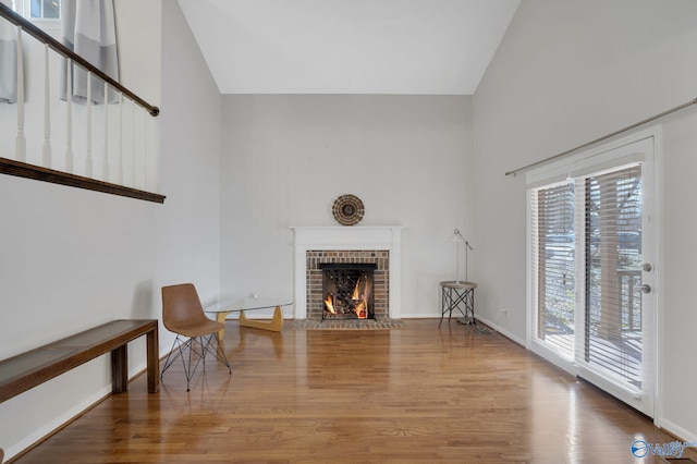 sitting room featuring a brick fireplace, baseboards, high vaulted ceiling, and wood finished floors