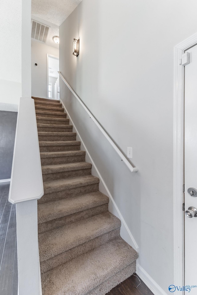 stairway featuring wood finished floors, visible vents, and baseboards