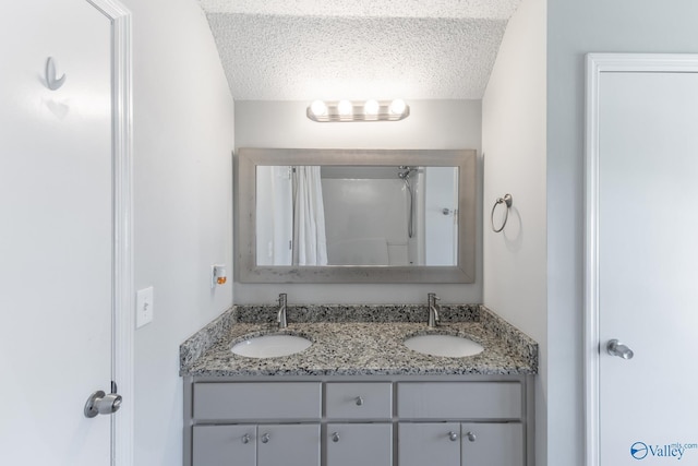 full bath with a sink, curtained shower, a textured ceiling, and double vanity