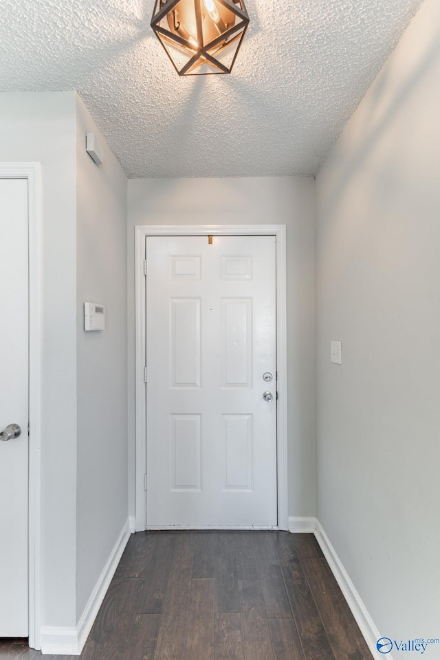 doorway to outside featuring baseboards, dark wood-style flooring, and a textured ceiling