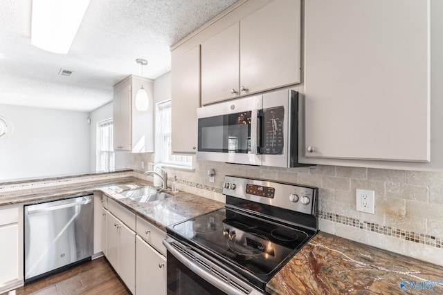 kitchen featuring backsplash, decorative light fixtures, appliances with stainless steel finishes, wood finished floors, and a sink