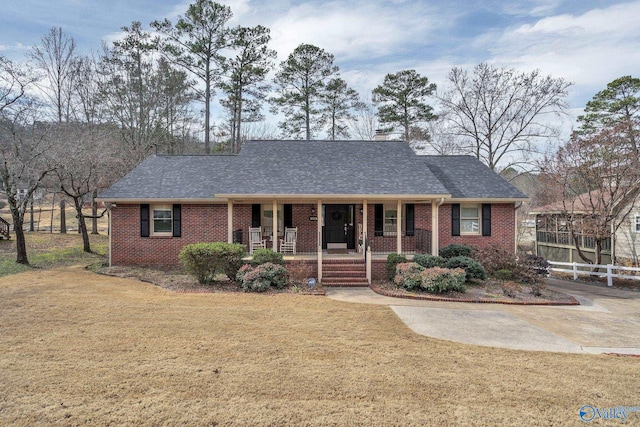 ranch-style home featuring covered porch, brick siding, and roof with shingles