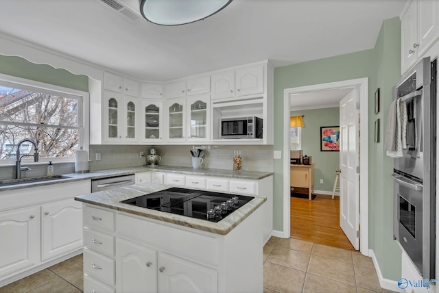 kitchen with a kitchen island, a sink, white cabinets, appliances with stainless steel finishes, and glass insert cabinets